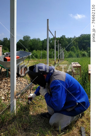 The welder welds a new metal frame for the fence around the house in the village. The welder welds a new metal frame for the fence around the house in the village. 76662150
