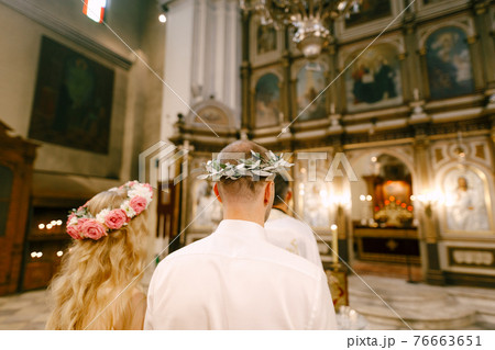 The priest, the groom and the bride in wreaths stand at the altar of the Church of St. Nicholas in Kotor during the wedding, back view The priest, the groom and the bride in wreaths stand at the altar of the Church of St. Nicholas in Kotor during the wedding, back view 76663651