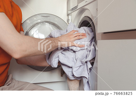 Man loading color clothes and towels into built-in washing machine Man loading color clothes and towels into built-in washing machine 76663825