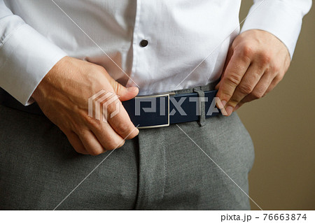 A man in blue pants and a white shirt buttoned a brown leather trouser belt. He has a watch on his hand. A man in blue pants and a white shirt buttoned a brown leather trouser belt. He has a watch on his hand. 76663874