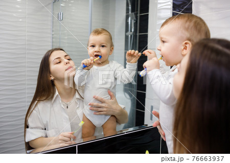 Full of proud mother looking at her baby son brushing his teeth in bathroom. Full of proud mother looking at her baby son brushing his teeth in bathroom. 76663937