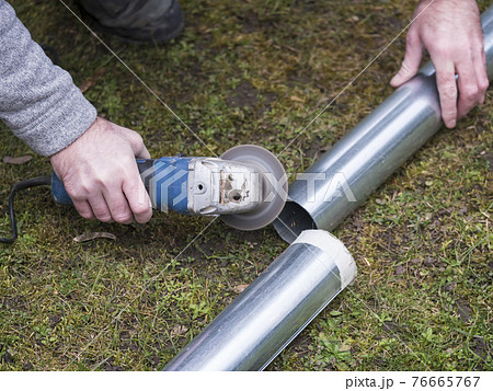 hands of man cutting the stove pipe, working with portable grinder machine on the grass hands of man cutting the stove pipe, working with portable grinder machine on the grass 76665767