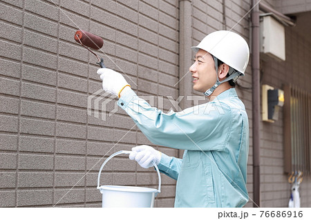 一軒家の外壁に塗装をする作業員の男性 76686916