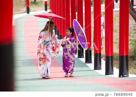woman and little girl in kimono holding umbrella walking into at the shrine red gate, in Japanese garden. woman and little girl in kimono holding umbrella walking into at the shrine red gate, in Japanese garden. 76689040