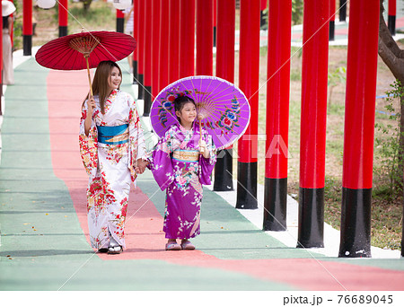 woman and little girl in kimono holding umbrella walking into at the shrine red gate, in Japanese garden. woman and little girl in kimono holding umbrella walking into at the shrine red gate, in Japanese garden. 76689045