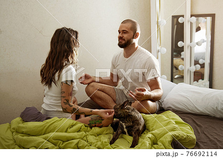 Couple practicing meditation exercises on the bed near their dog at home 76692114