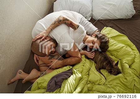 Spouses spending time with their dog while laying on the bed 76692116