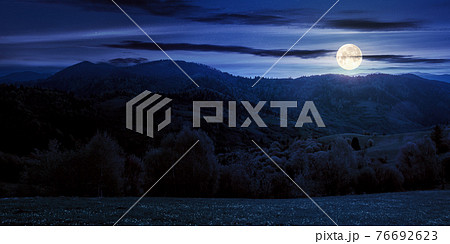 rolling rural mountain landscape at night. gorgeous nature scenery in spring. clouds on the sky in full moon light 76692623