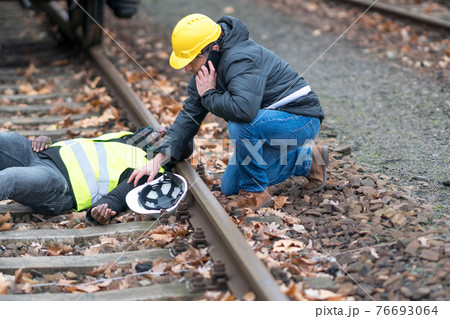 African American railroad engineer injured in an accident at work on the railway tracks. His coworker using his cell phone to call 911 76693064