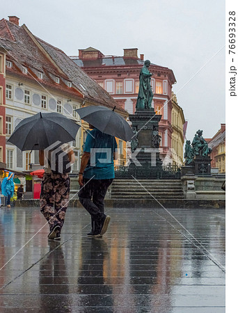 People with umbrella passing by Erzherzog Johann fountain at Hauptplatz (main square) in a rainy day, in Graz, Styria region, Austria. 76693328