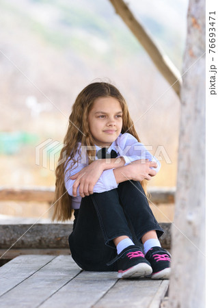 A girl sits on a wooden table and looks into the distance happily and dreamily 76693471
