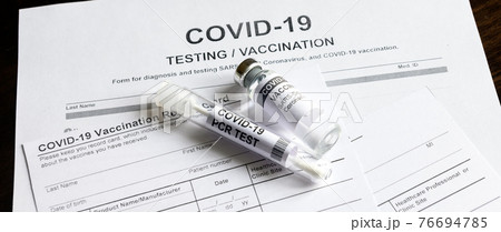 COVID-19 vaccine vial and PCR test kit on medical forms in clinic COVID-19 vaccine vial and PCR test kit on medical forms in clinic 76694785