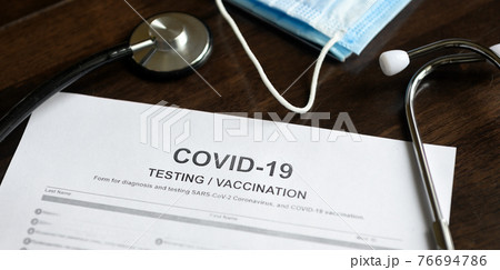 COVID-19 testing and vaccination form and stethoscope on desk 76694786