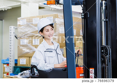 ヘルメットを被りフォークリフトを操作する女性 76696379