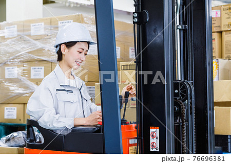ヘルメットを被りフォークリフトを操作する女性 76696381