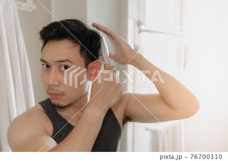 Man is combing his hair in the bathroom. 76700310