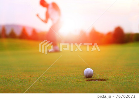 Golfing game. Asian man golfer action to win after winner long putting golf ball on the green golf, outdoors sunset time , Pro golfer putting golf ball in to the hole. 76702073