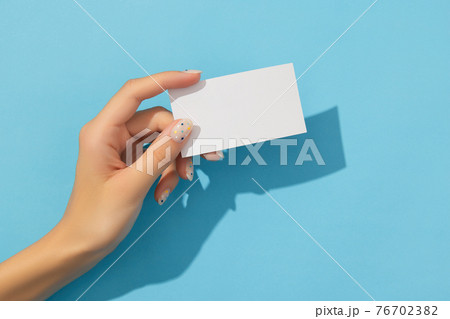 Manicured womans hand holding business on blue background Manicured womans hand holding business on blue background 76702382