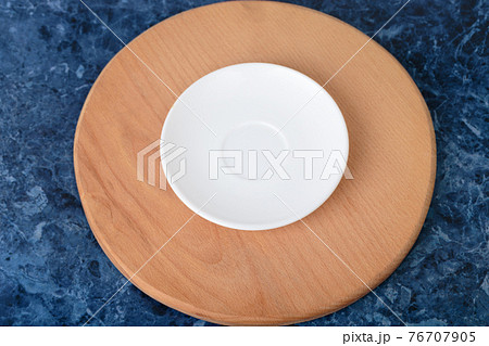 The porcelain saucer is on a wooden cutting board. 76707905
