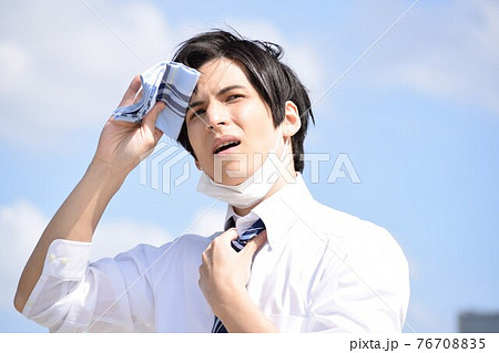 暑くてマスクを外してハンカチで汗を拭いている若い男性 76708835