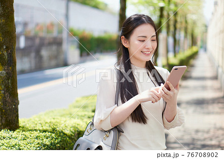 キャンパス前でスマホを持つ大学生 76708902
