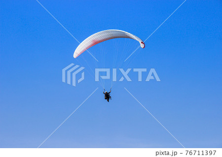 Tourist flying on a paraglider flying in the blue sky on a bight day. The sportsman paragliding. 76711397