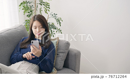 部屋でリラックスしてスマホを見る女性 76712264