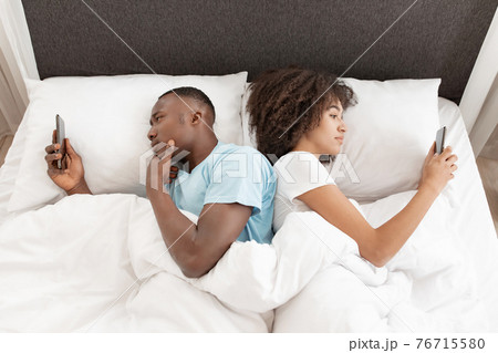 Awake using phone for chat, couple in quarrel, lying on bed back to back, using smartphones 76715580