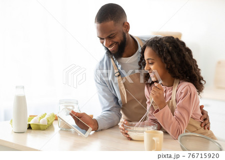 Black man and girl cooking in the kitchen using tablet Black man and girl cooking in the kitchen using tablet 76715920