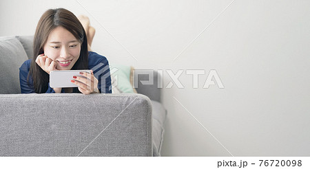 ソファに寝転がってスマホを見る女性 76720098
