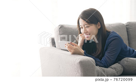 ソファに寝転がってスマホを見る女性 ソファに寝転がってスマホを見る女性 76720099