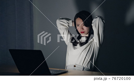 暗い部屋でパソコン作業をする女性の写真素材