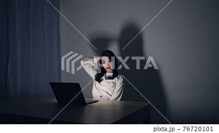 暗い部屋でパソコン作業をする女性の写真素材