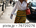 Detail of a fashionable outfit woman wearing white shirt, yellow and green skirt and red handbag 76720276