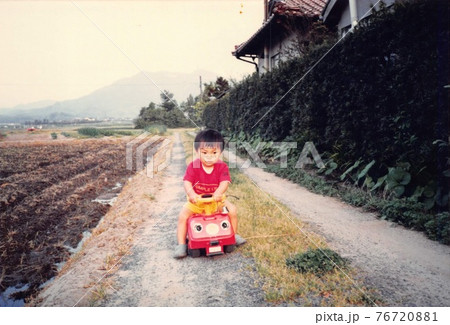 昔のフィルム写真　田舎のあぜ道で小さな車に乗る男の子 76720881