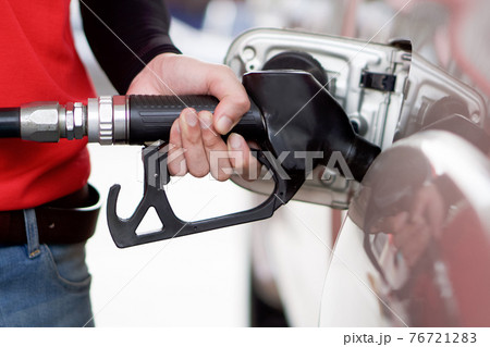 Gas station worker in red uniform filling up bronze pickup truck tank. Closeup hand holding black gas pump nozzle. 76721283