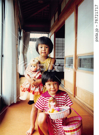 昔のフィルム写真　家の廊下で人形ごっこをして遊ぶ二人の女の子の姉妹 76721717