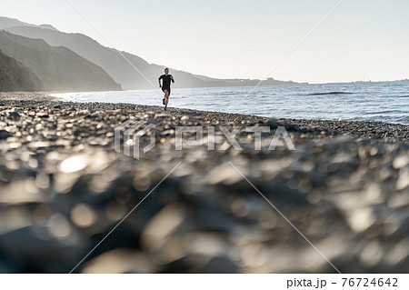 Man run on the beach, mountains background 76724642