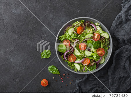 Fresh healthy vegetarian vegetables salad with tomatoes and cucumber, red onion and spinach in grey bowl plate on dark background. Fresh healthy vegetarian vegetables salad with tomatoes and cucumber, red onion and spinach in grey bowl plate on dark background. 76725480