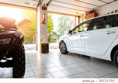 Home suburban countryside modern car and ATV double garage interior with wooden shelf, tools and equipment stuff storage warehouse indoors against sun light. Vehicle parked house parking background Home suburban countryside modern car and ATV double garage interior with wooden shelf, tools and equipment stuff storage warehouse indoors against sun light. Vehicle parked house parking background 76725797
