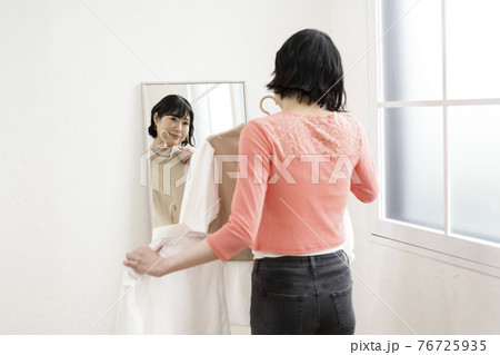 どの服にしようか鏡を見ながら選ぶ女性 76725935