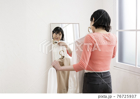 どの服にしようか鏡を見ながら選ぶ女性 76725937