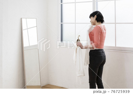 どの服にしようか鏡を見ながら選ぶ女性 76725939
