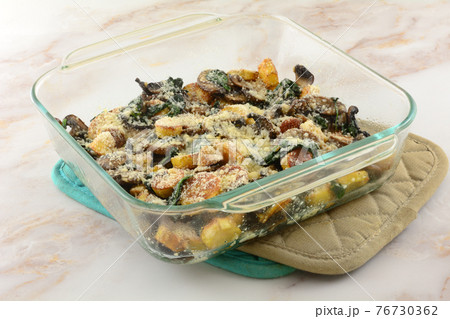 Baked cheese casserole of potatoes, spinach, and mushrooms in glass baking dish on two pot holders Baked cheese casserole of potatoes, spinach, and mushrooms in glass baking dish on two pot holders 76730362