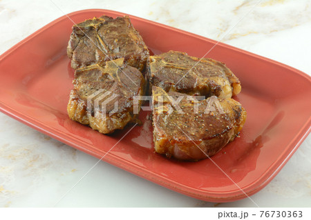 Four baked lamb chops with spice rub on red serving plate 76730363