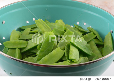 Freshly rinsed raw snow peas with ends trimmed off draining in blue colander 76730667