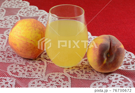 Peach juice in drinking glass and fresh raw peaches on pink heart lace table runner on red tablecloth Peach juice in drinking glass and fresh raw peaches on pink heart lace table runner on red tablecloth 76730672
