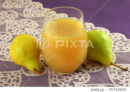 Pear juice in a drinking glass with fresh raw bartlett pears on pink lace table runner on purple tablecloth 76730695