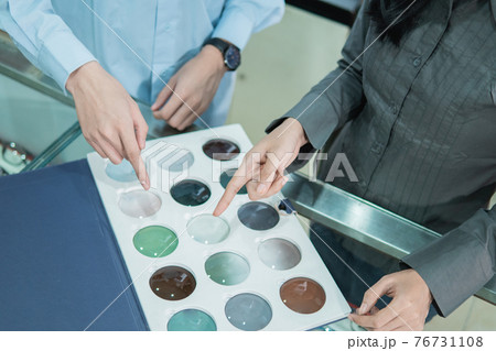 the hands of a shopkeeper and a customer by finger pointing to a sample of lenses when selecting the type of lens the hands of a shopkeeper and a customer by finger pointing to a sample of lenses when selecting the type of lens 76731108