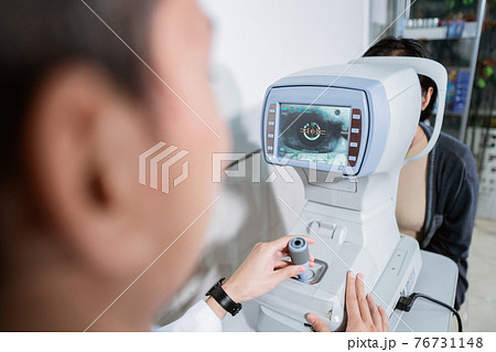 a male ophthalmologist is operating an eye computer for a female patient to examine the patient's eyes 76731148